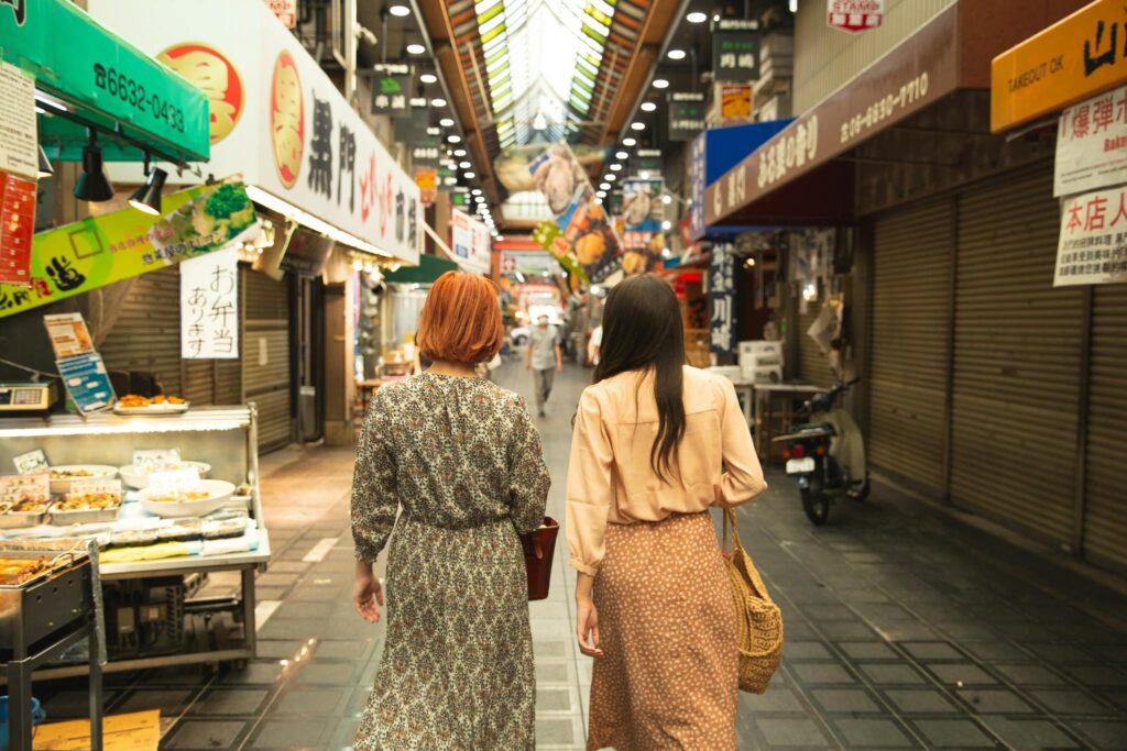 Back view of unrecognizable trendy female travelers in stylish clothes walking in traditional famous Nishiki Market in Kyoto